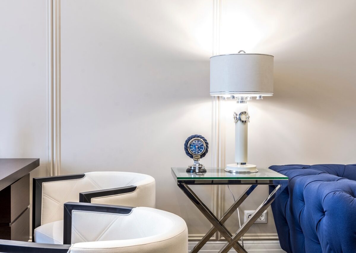 about-us-02 Interior of contemporary living room with small table and lamp near sofa and armchairs