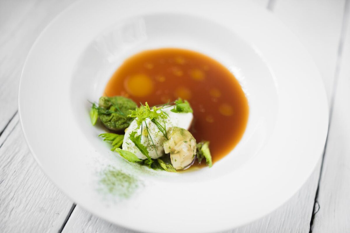 Elegant gourmet dish featuring vegetables in a rich broth served in a white plate.