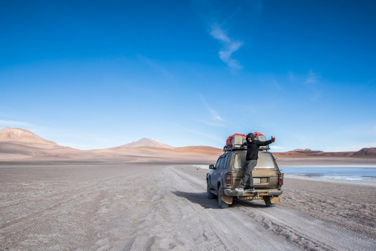 services-02 SUV in a barren desert with a man standing on the trunk, capturing adventure spirit.